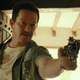 Mark Wahlberg, in an unbuttoned floral shirt and bad mustache, aims a gun at Tom Holland.